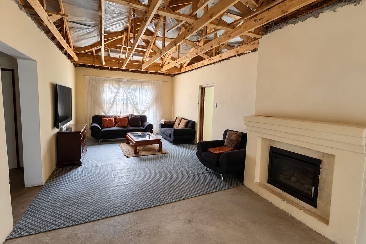 Living room featuring a built-in fireplace, concrete flooring, and exposed timber roof trusses, currently undergoing renovation with an unfinished ceiling.