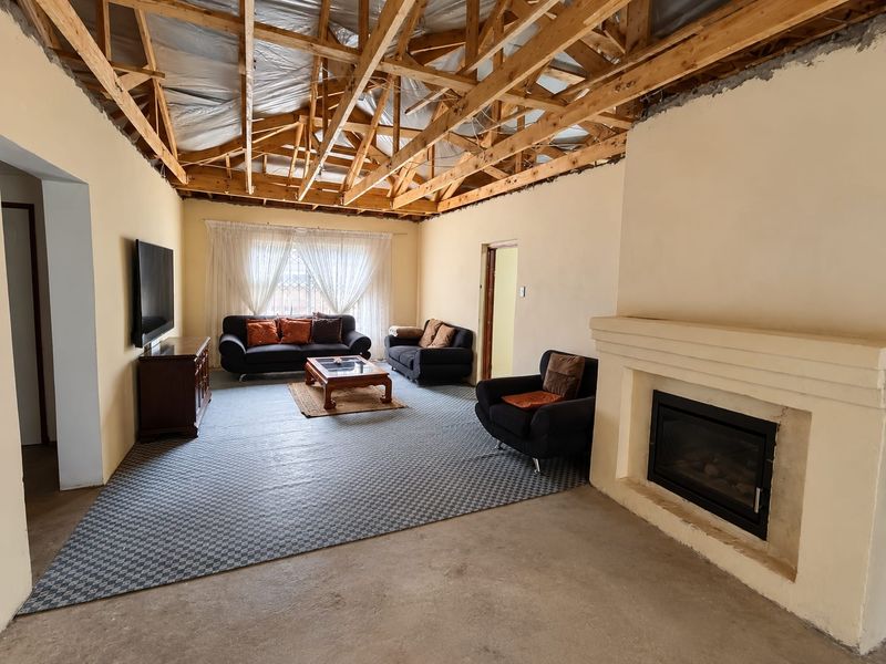 Living room featuring a built-in fireplace, concrete flooring, and exposed timber roof trusses, currently undergoing renovation with an unfinished ceiling.