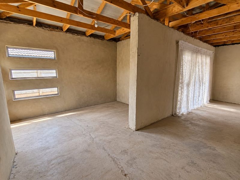 An unfinished interior space featuring exposed timber roof trusses, raw plastered walls, and cement screed flooring, offering a blank canvas for renovation.