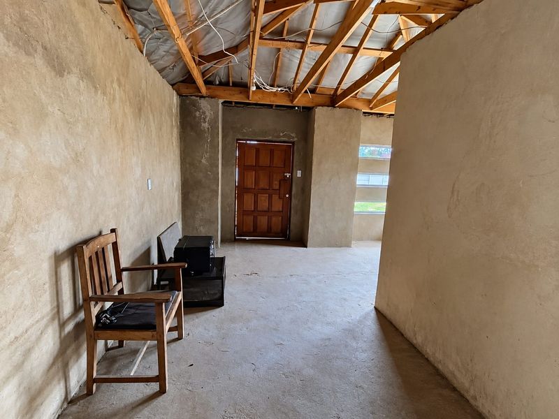 An unfinished interior space featuring exposed timber roof trusses, cement flooring, and plastered walls, offering a blank canvas for renovation.