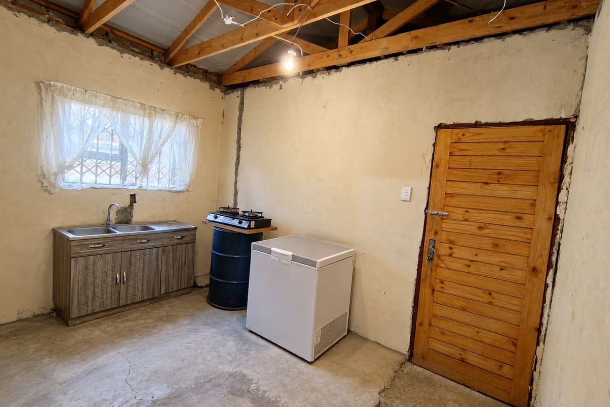 A rustic kitchen area featuring exposed timber roof trusses, concrete flooring, and basic cabinetry with a sink, requiring significant finishing and renovation.