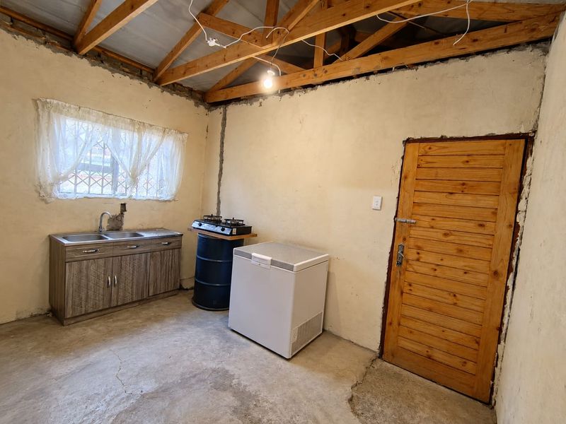 A rustic kitchen area featuring exposed timber roof trusses, concrete flooring, and basic cabinetry with a sink, requiring significant finishing and renovation.