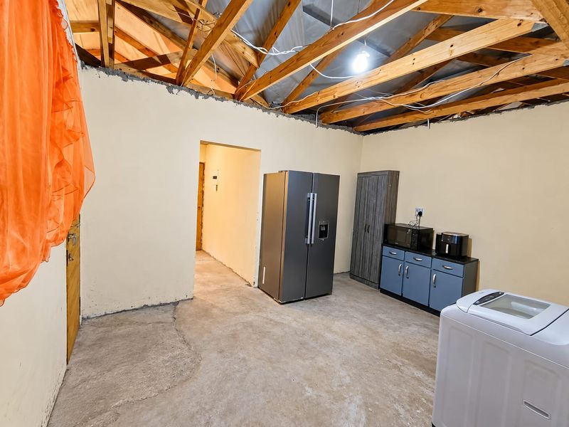 Utility space featuring exposed timber roof trusses, concrete flooring, and basic cabinetry, currently used as a laundry and storage area.
