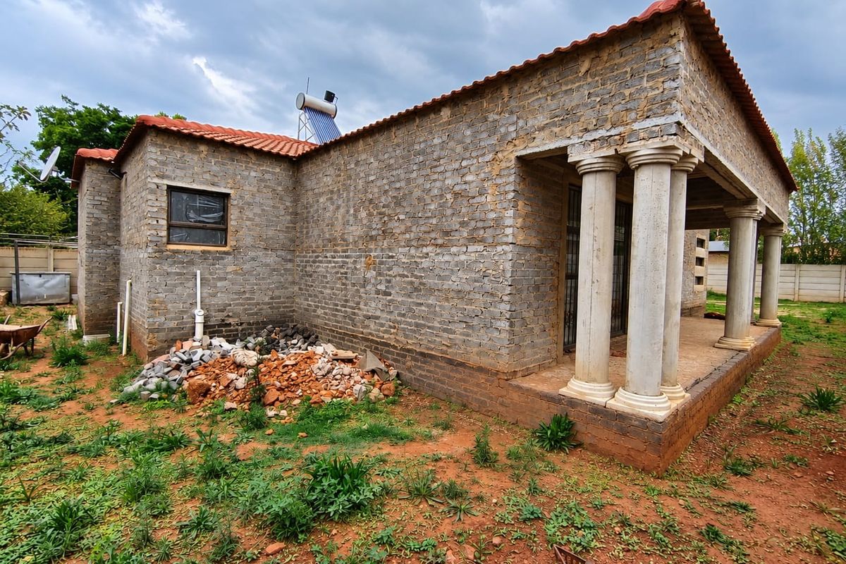 Rear view of a house under construction featuring unfinished brick walls, a covered patio with concrete columns, and a solar water heating system.
