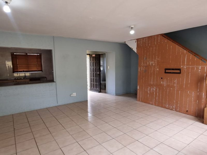 An open-plan living area featuring tiled flooring, a staircase with a wooden balustrade, and a convenient serving hatch connecting to the kitchen.