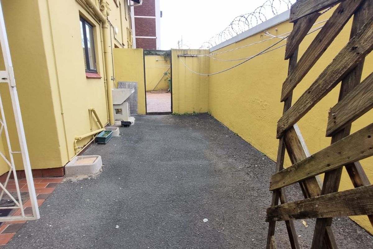 A private rear courtyard area featuring a concrete wash basin, security boundary walls with razor wire, and a secure access gate.