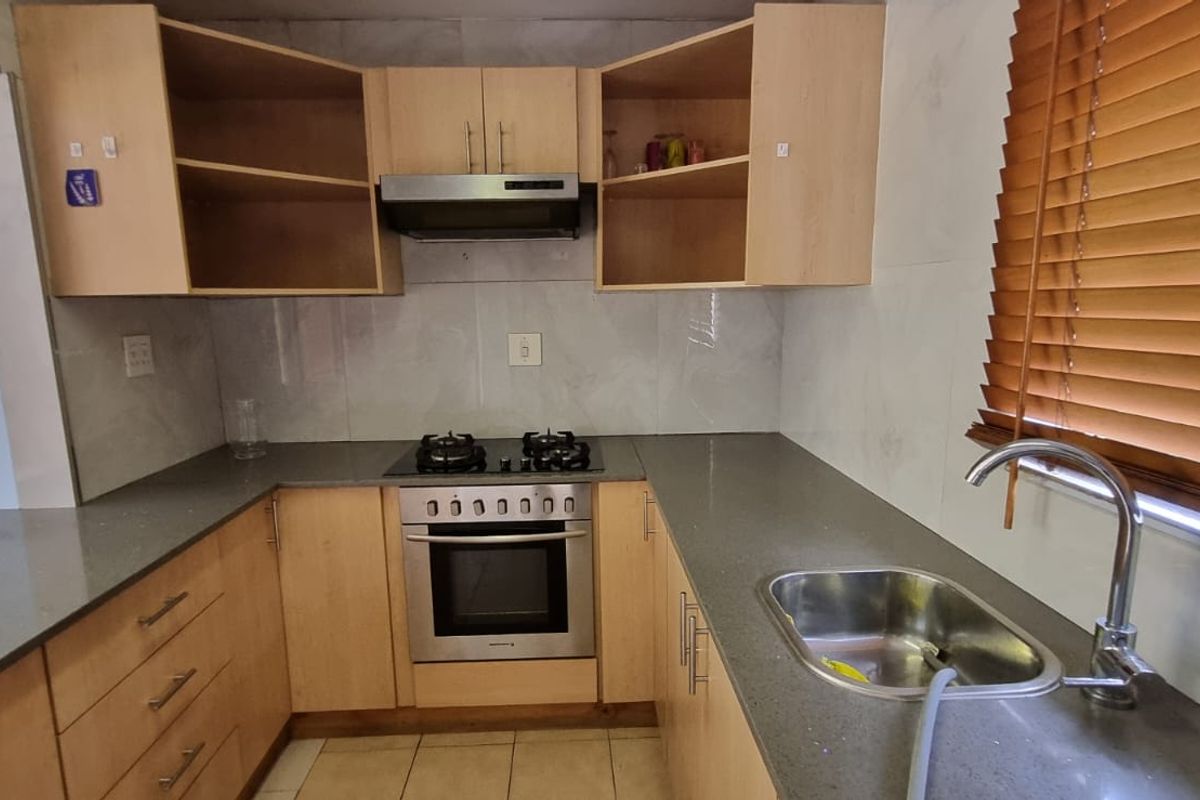A functional kitchen featuring light wood cabinetry, stone countertops, a gas hob with extractor, and a stainless steel sink with a tiled backsplash.