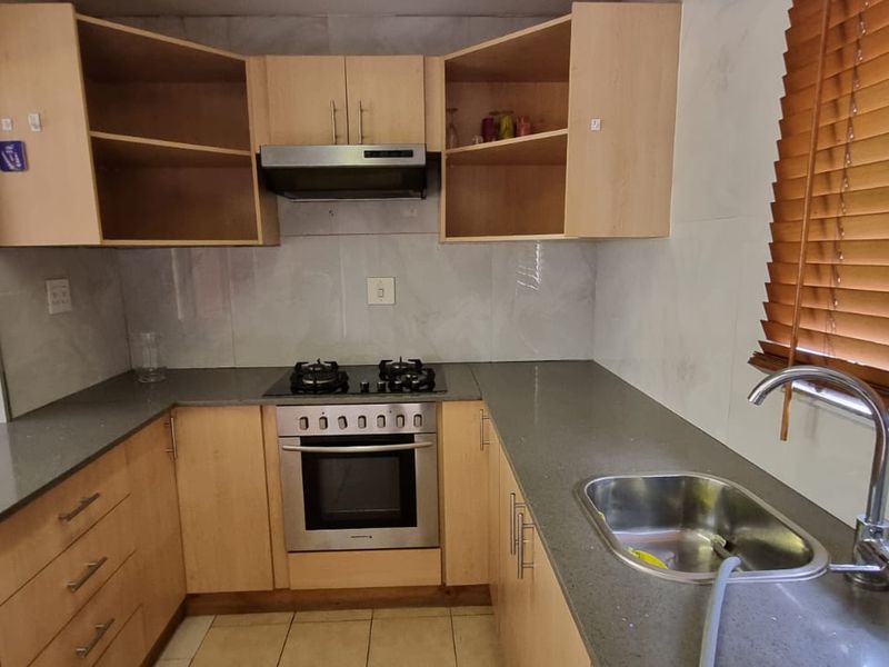 A functional kitchen featuring light wood cabinetry, stone countertops, a gas hob with extractor, and a stainless steel sink with a tiled backsplash.