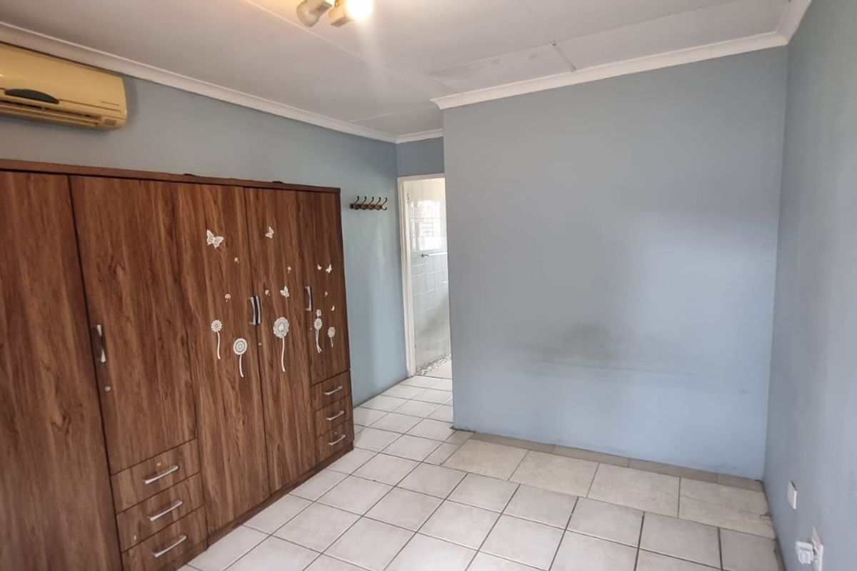 A bedroom featuring tiled flooring, a large built-in wardrobe, and a wall-mounted air conditioning unit.