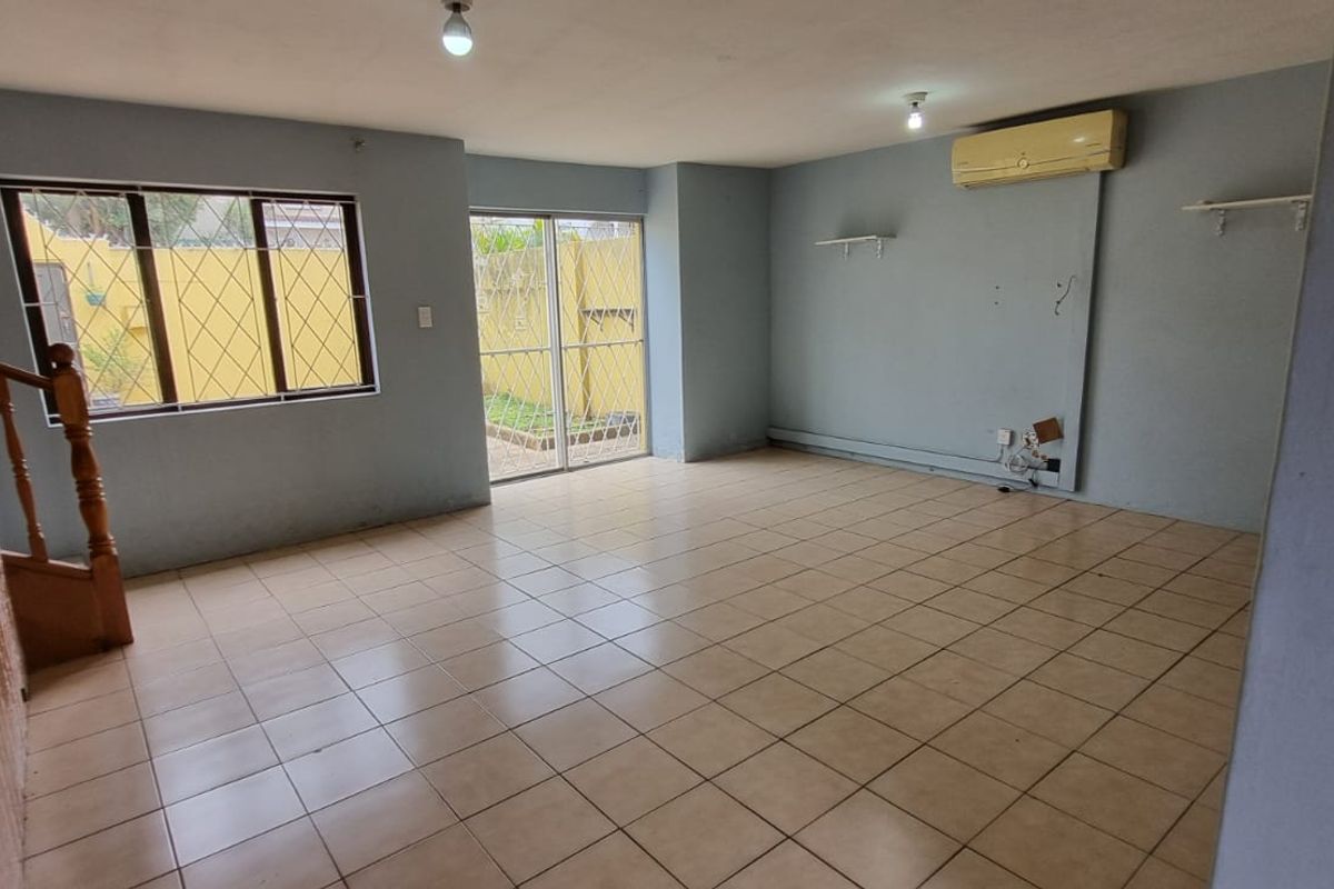 An empty, open-plan living area featuring tiled floors, a wooden staircase, and direct access to an outdoor space through a sliding glass door.