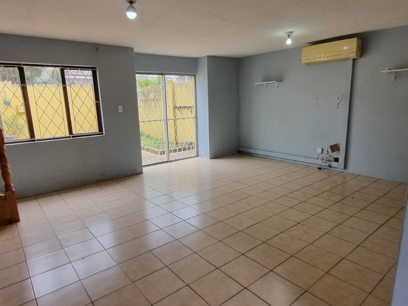 An empty, open-plan living area featuring tiled floors, a wooden staircase, and direct access to an outdoor space through a sliding glass door.