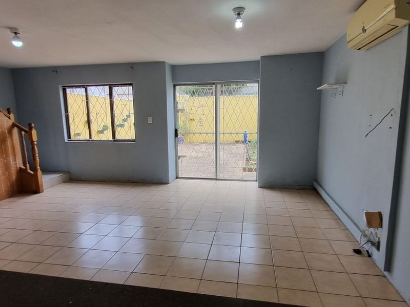 Spacious living area featuring tiled flooring, a staircase, and direct access to the rear exterior through a sliding glass door with security bars.