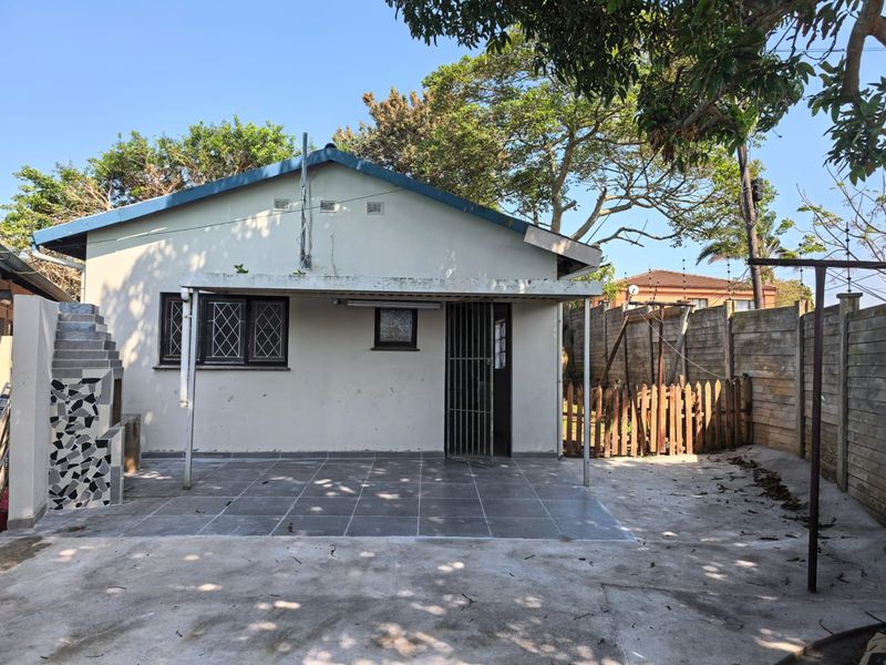 Rear exterior view of the cottage featuring a tiled patio area, built-in braai, and enclosed garden space with perimeter walling.