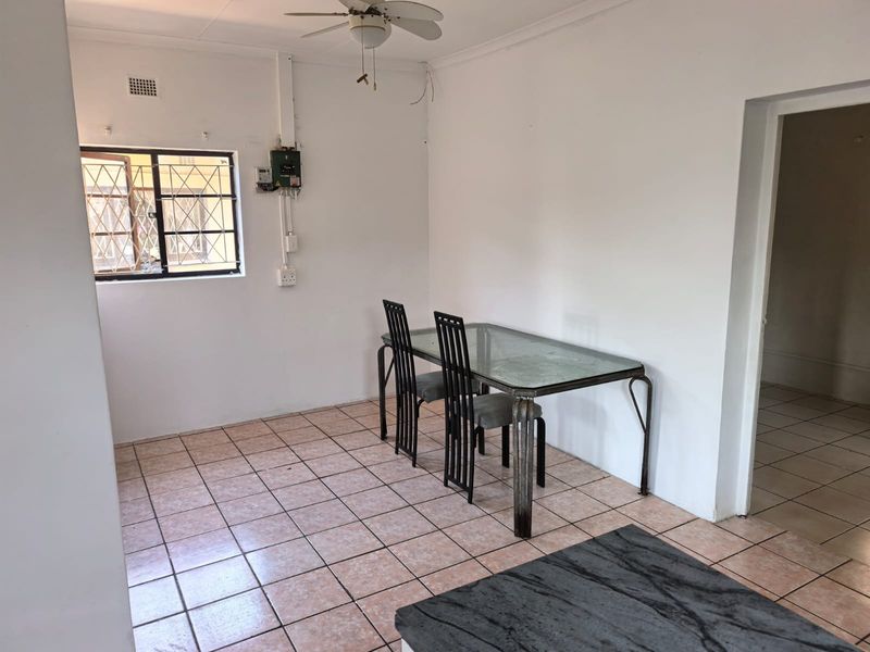 A dining area featuring tiled flooring, a ceiling fan, and security bars on the window, with visible electrical infrastructure.
