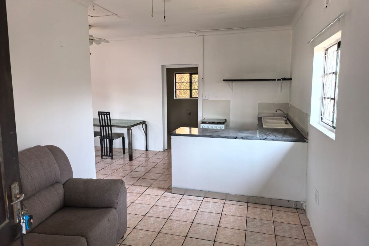 Open-plan living and kitchen area featuring tiled flooring, a functional kitchen layout with a built-in stove, and security bars on the windows.