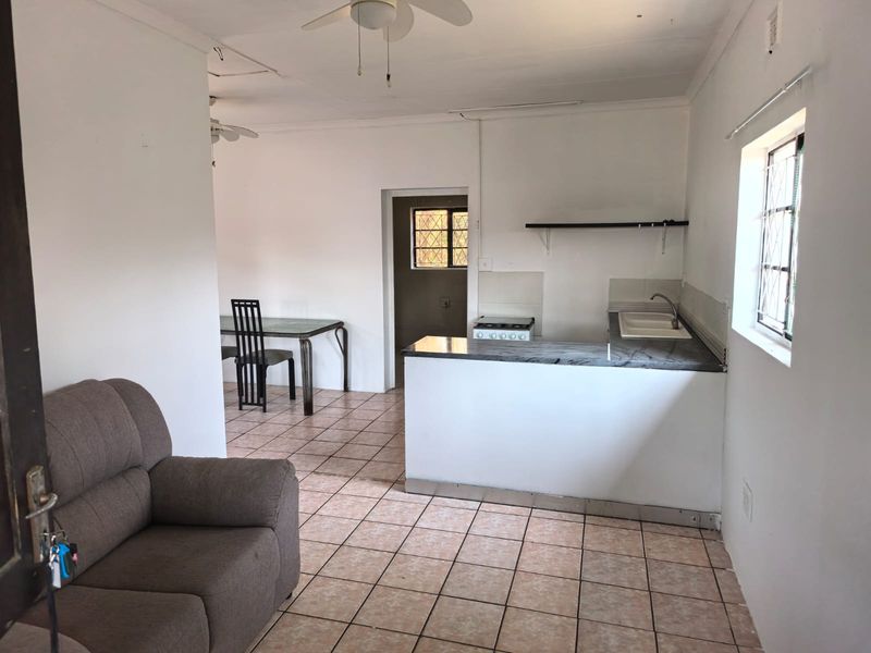 Open-plan living and kitchen area featuring tiled flooring, a functional kitchen layout with a built-in stove, and security bars on the windows.