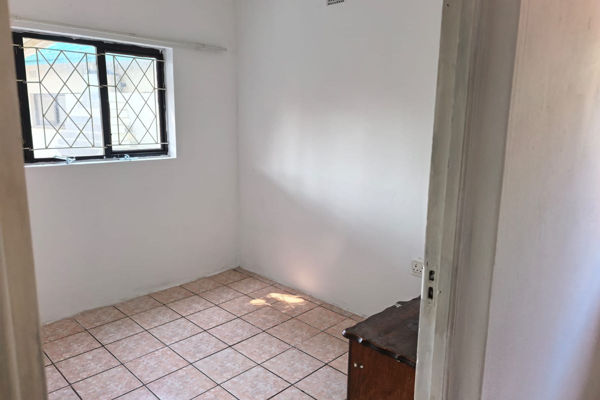 A vacant bedroom featuring tiled flooring, a window with security bars, and a ventilation grille, offering a blank canvas for potential updates.