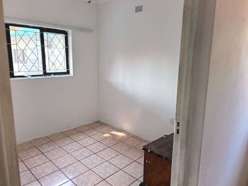 A vacant bedroom featuring tiled flooring, a window with security bars, and a ventilation grille, offering a blank canvas for potential updates.