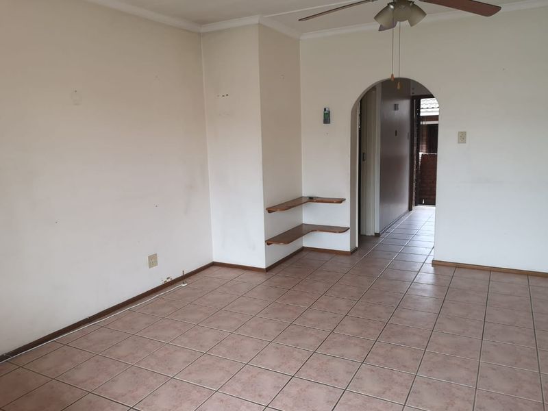 An empty living room featuring tiled flooring, a ceiling fan, and a characterful archway leading to a hallway.