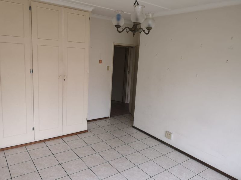 An empty bedroom featuring built-in cupboards, tiled flooring, and a central light fixture, requiring minor cosmetic wall repairs.
