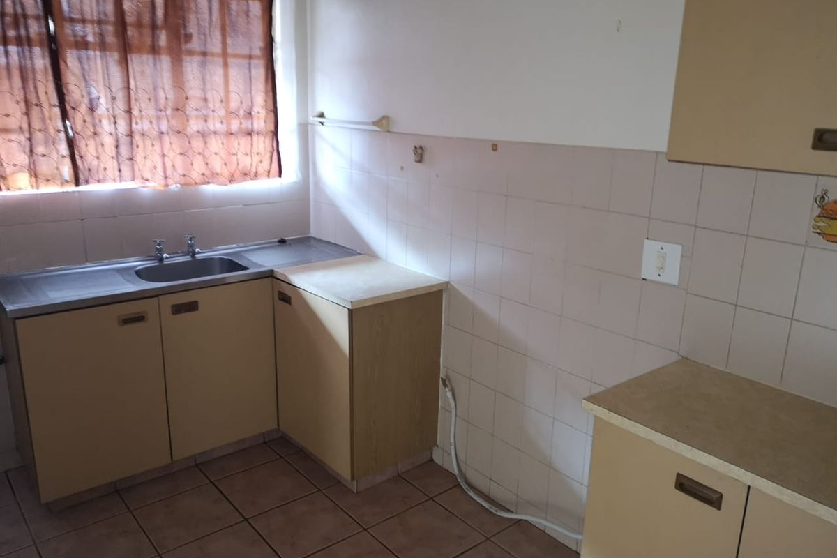 A dated kitchen featuring laminate cabinetry, tiled splashbacks, and a stainless steel sink, offering a blank canvas for potential renovation and modernization.