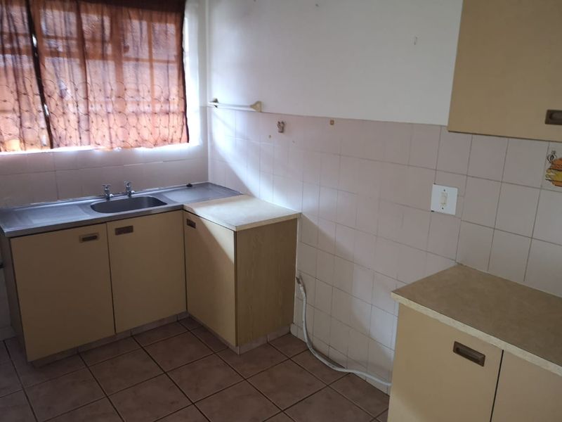 A dated kitchen featuring laminate cabinetry, tiled splashbacks, and a stainless steel sink, offering a blank canvas for potential renovation and modernization.