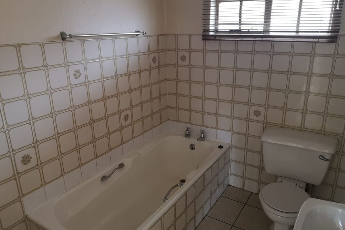 A dated bathroom featuring a built-in bathtub, toilet, and bidet with original tiled finishes and a window with blinds.
