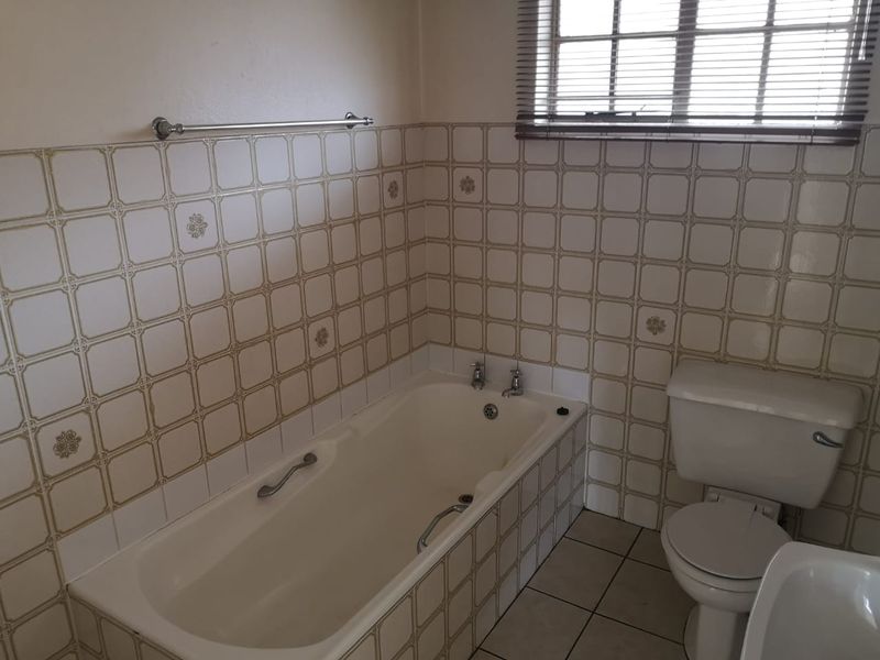 A dated bathroom featuring a built-in bathtub, toilet, and bidet with original tiled finishes and a window with blinds.