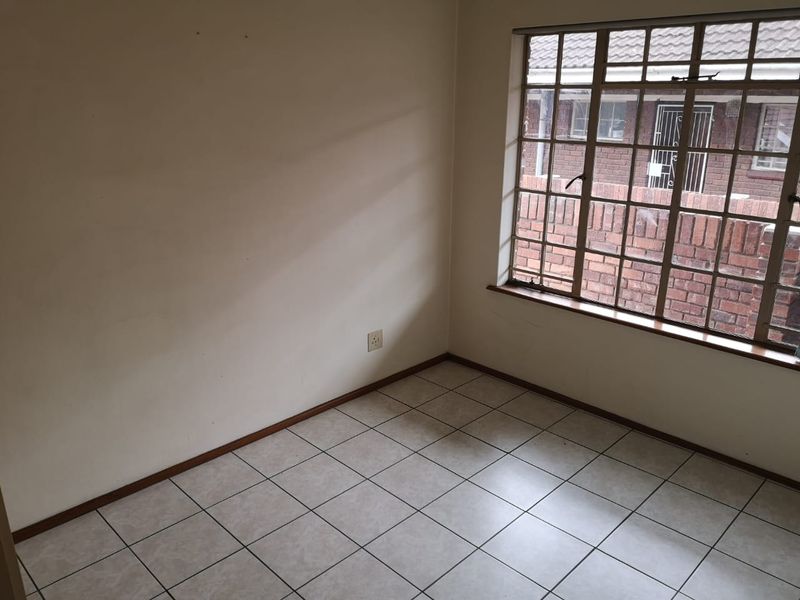 An empty bedroom featuring tiled flooring, a window with security bars, and neutral wall finishes, ready for personalization.