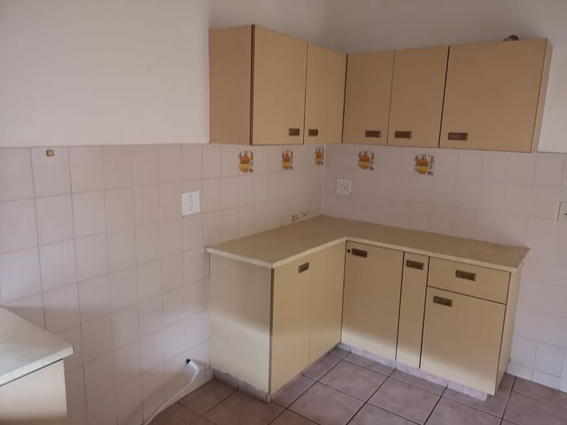 A compact, empty kitchen featuring dated laminate cabinetry, tiled splashbacks, and tiled flooring, offering a blank canvas for modern renovation.