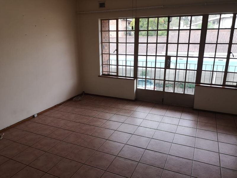 An empty living room featuring tiled flooring and large grid-pattern windows that provide natural light and access to the exterior.