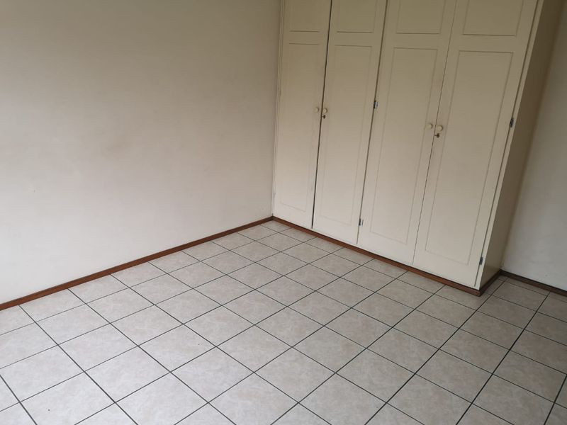 An empty bedroom featuring neutral tiled flooring and built-in cupboards, offering a clean and versatile space ready for personalization.