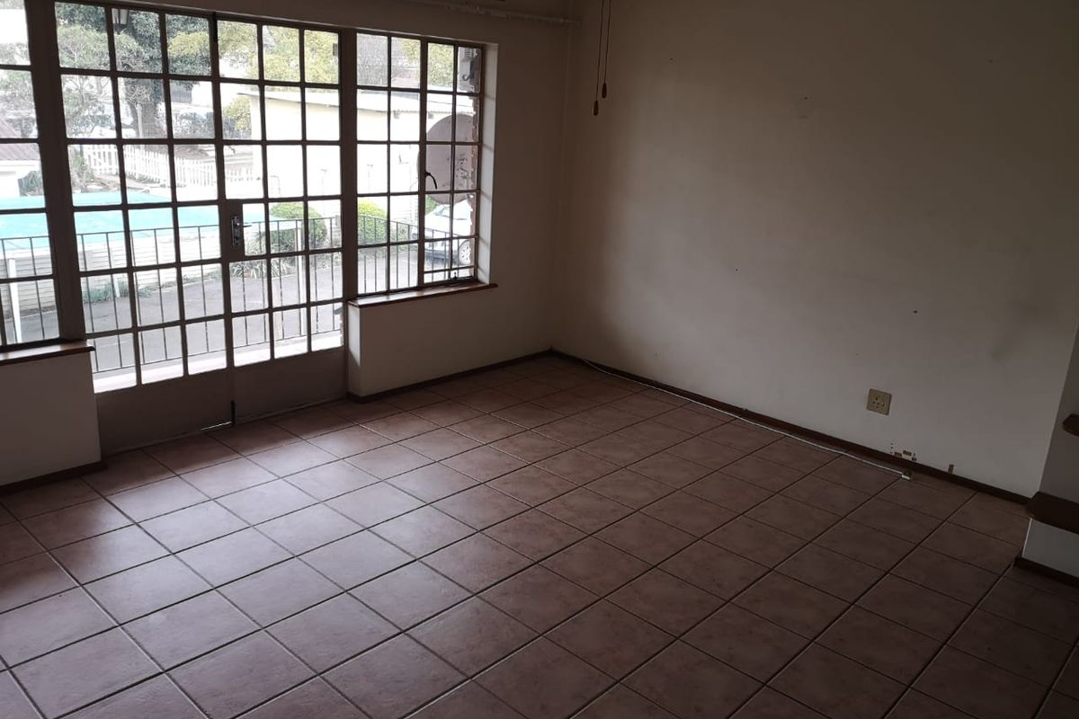 An empty living room featuring tiled flooring, a ceiling fan, and large steel-framed windows providing natural light and access to the exterior.