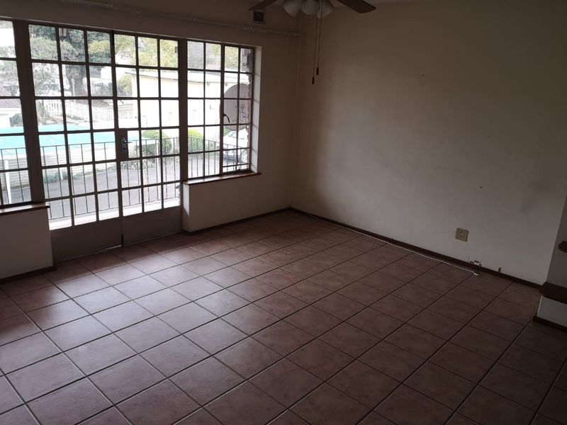 An empty living room featuring tiled flooring, a ceiling fan, and large steel-framed windows providing natural light and access to the exterior.