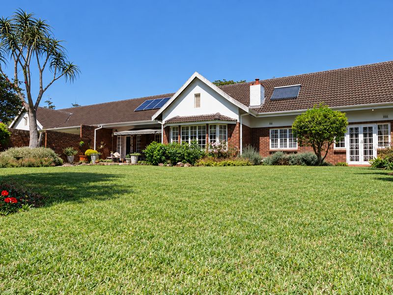 Spacious rear garden view of a well-maintained townhouse featuring a brick facade, tiled roof, solar water heating panels, and established landscaping.