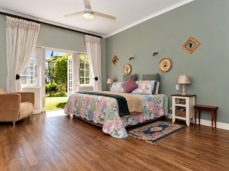 Spacious bedroom featuring laminate flooring, a ceiling fan, and direct access to the garden through classic French doors.
