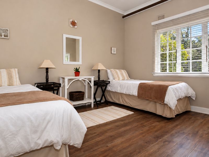A well-maintained bedroom featuring laminate flooring, neutral wall tones, and a large window with venetian blinds allowing for natural light.