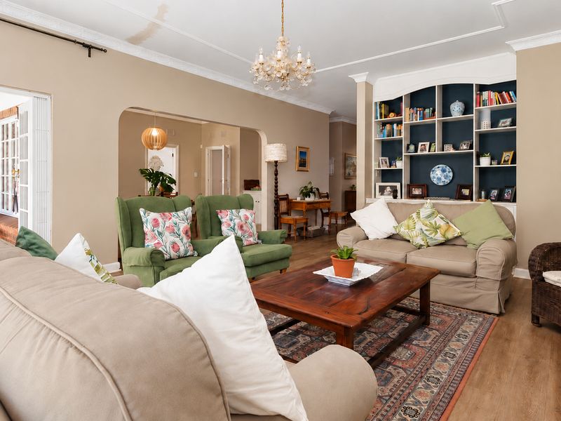 Spacious living room featuring a built-in shelving unit, crown molding, and laminate flooring, with an open-plan flow leading to an outdoor patio area.