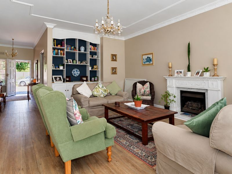 Spacious living room featuring a classic fireplace with mantelpiece, built-in shelving, elegant crown molding, and warm laminate flooring.