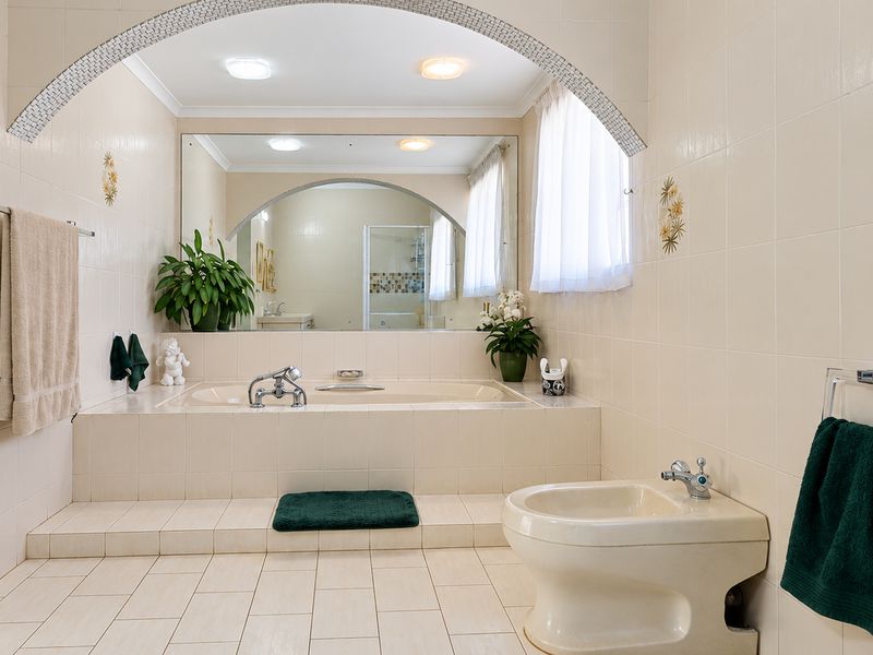 Spacious bathroom featuring a built-in bathtub, bidet, and decorative archway with neutral wall and floor tiling.