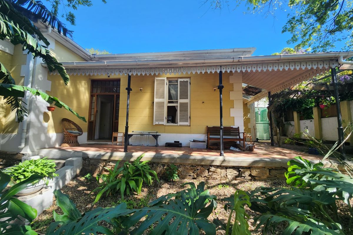 A rear view of a traditional house featuring a covered patio with decorative fretwork, terracotta tiling, and a stone retaining wall.