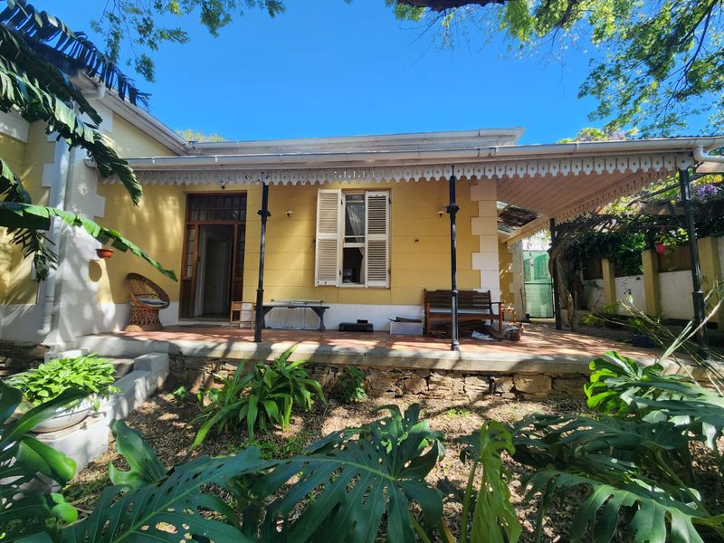 A rear view of a traditional house featuring a covered patio with decorative fretwork, terracotta tiling, and a stone retaining wall.