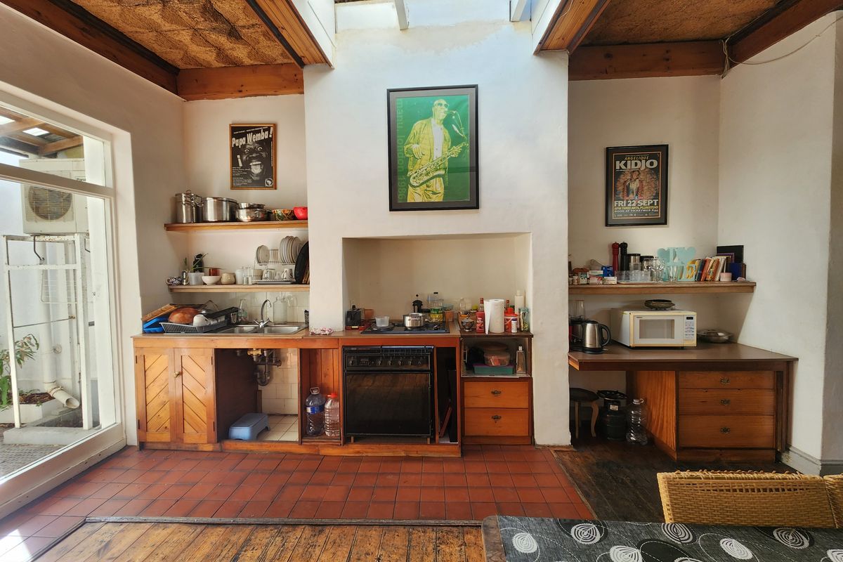 Rustic kitchen featuring exposed timber beams, a skylight, terracotta flooring, and built-in wooden cabinetry with open shelving and integrated cooking appliances.