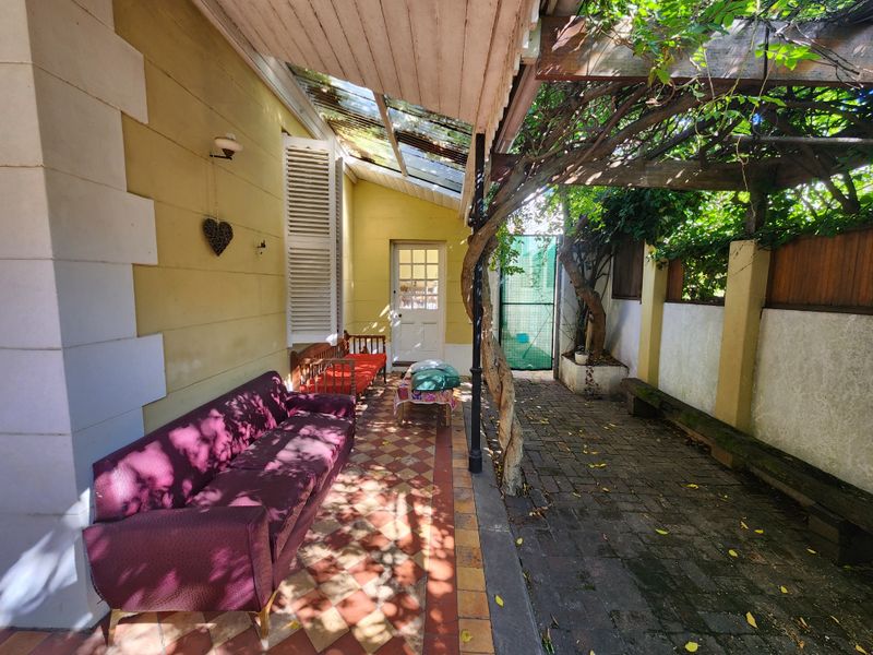 A covered patio area featuring a timber pergola, tiled flooring, and brick paving, providing a shaded outdoor space with direct access to the garden.