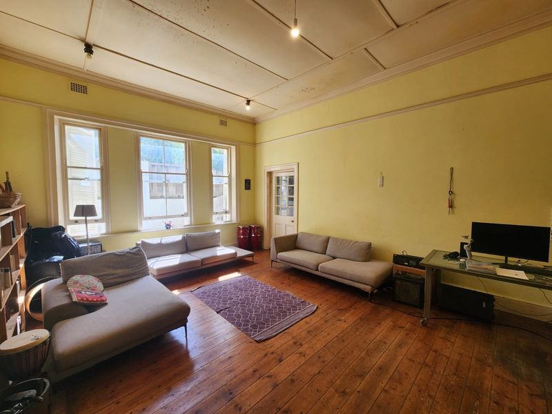 Spacious living room featuring original timber flooring, high ceilings with period detailing, and large sash windows allowing for ample natural light.
