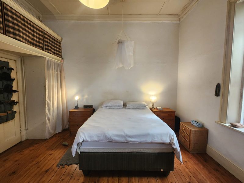 A bedroom featuring original hardwood flooring, high ceilings, and built-in storage, showing signs of wear and requiring cosmetic updates.