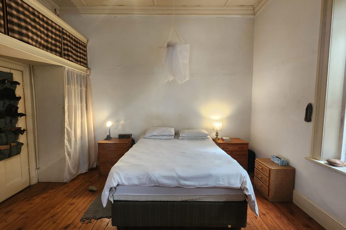 A bedroom featuring original hardwood flooring, high ceilings, and built-in storage, showing signs of wear and requiring cosmetic updates.