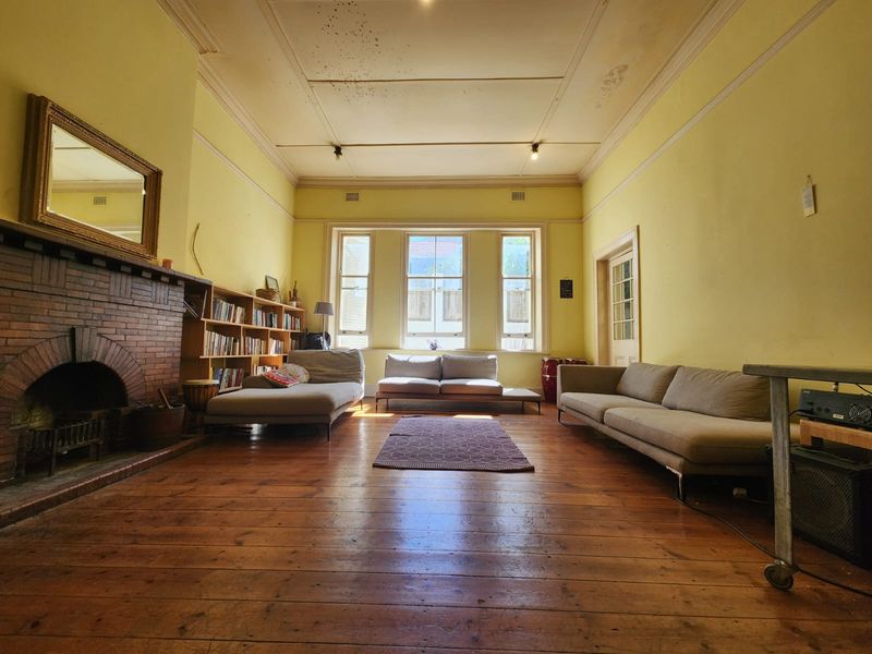 Spacious living room featuring original timber flooring, a classic brick fireplace, and built-in shelving, requiring cosmetic updates to the ceiling and walls.