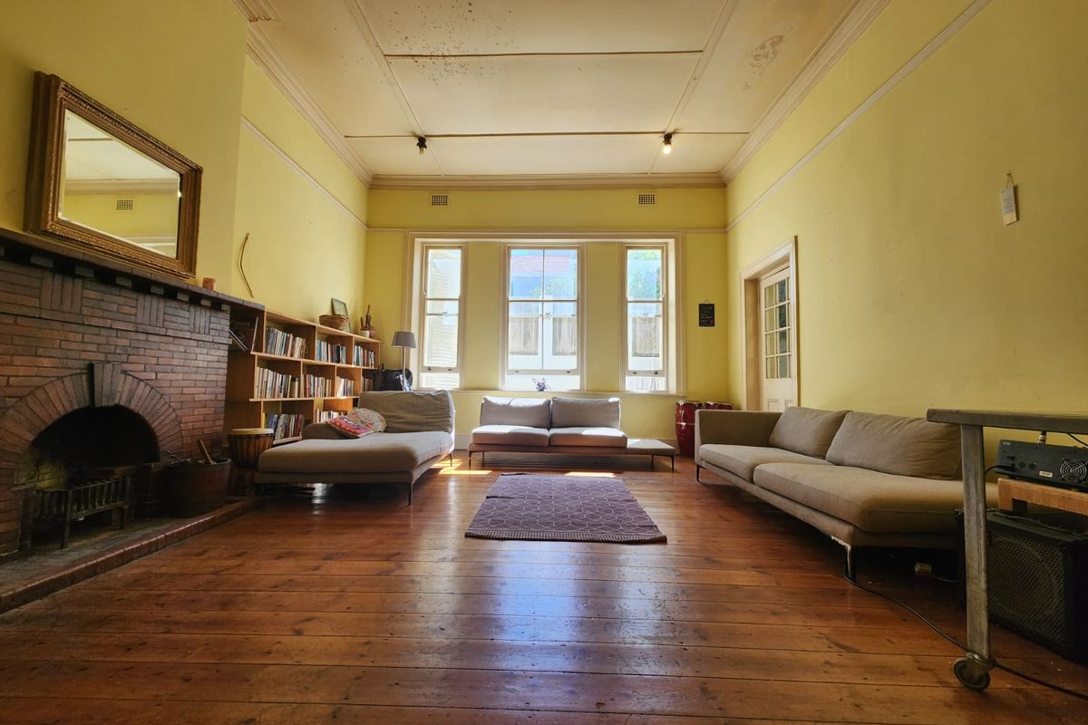 Spacious living room featuring original timber flooring, a classic brick fireplace, and built-in shelving, requiring cosmetic updates to the ceiling and walls.