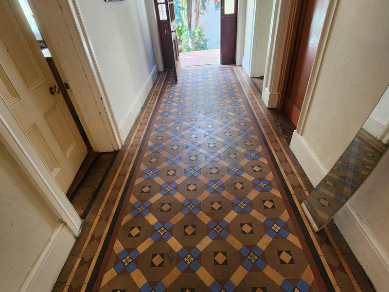 A bright hallway featuring classic, well-preserved encaustic patterned floor tiles leading to an open exterior doorway.